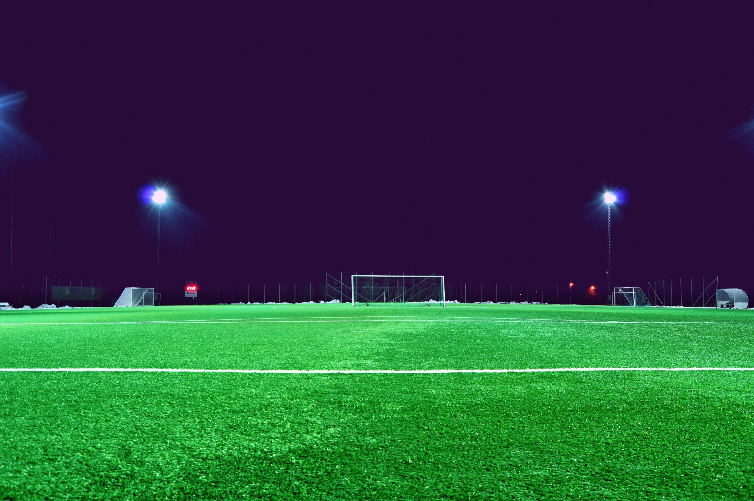 A wide-angle commercial shot of a massive professional football stadium under bright floodlights with a pristine green pitch.