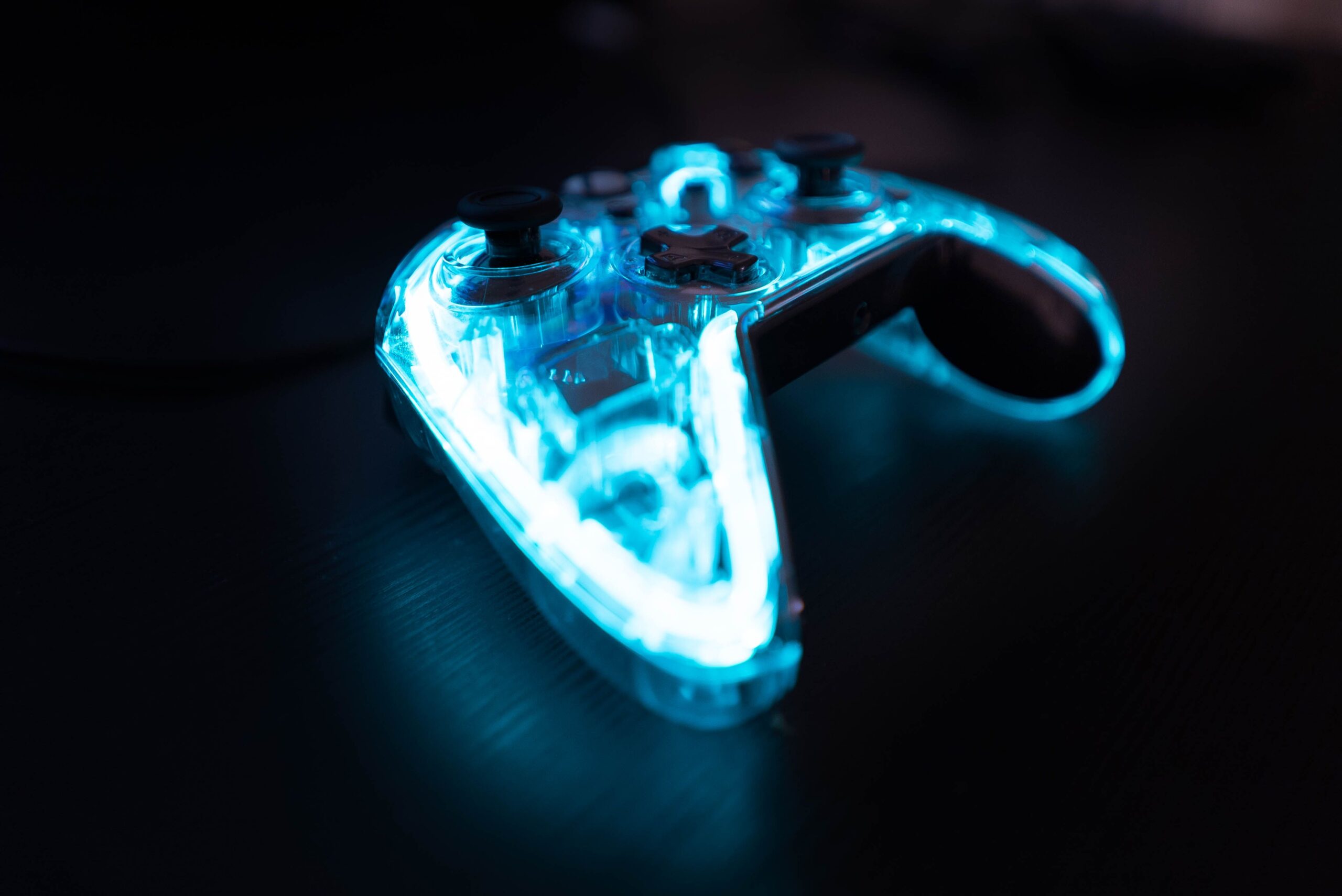 A professional entertainment journalism photograph displaying a high-end matte black gaming console controller surrounded by sharp ambient neon laser patterns