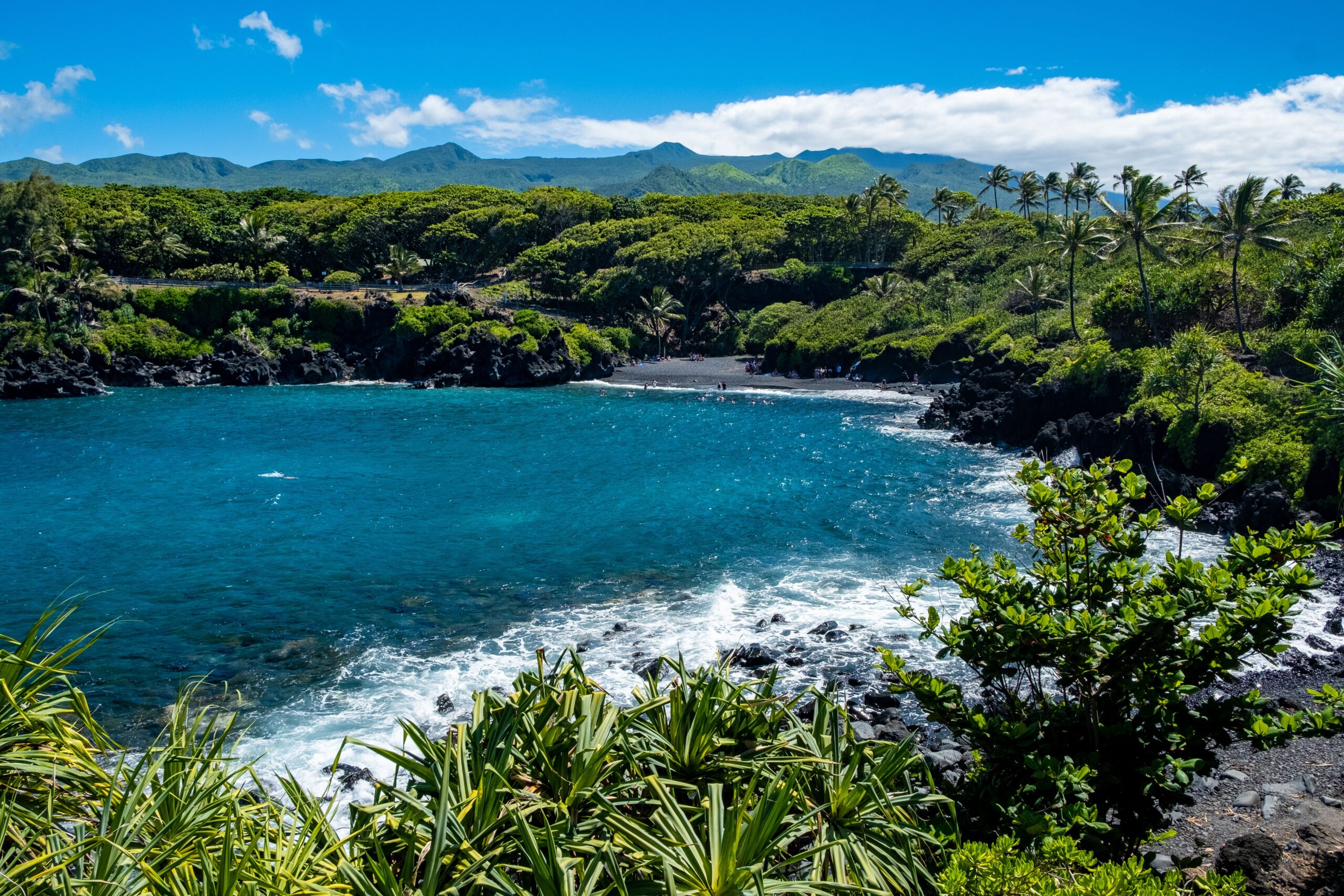An aerial panoramic commercial shot showing rugged volcanic cliffs meeting deep turquoise ocean waters under a clear blue sky.