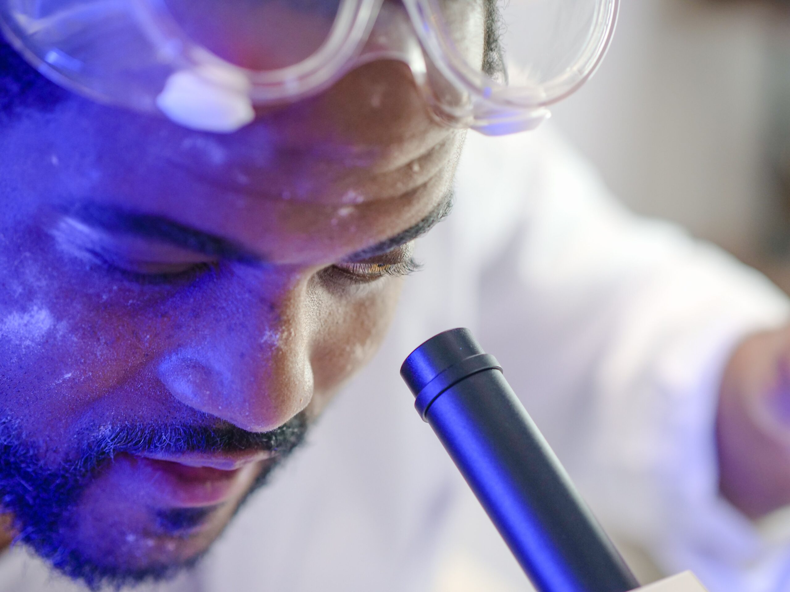A professional scientific macro photograph of a modern laboratory microscope with a glowing blue light focusing on a glass diagnostic slide