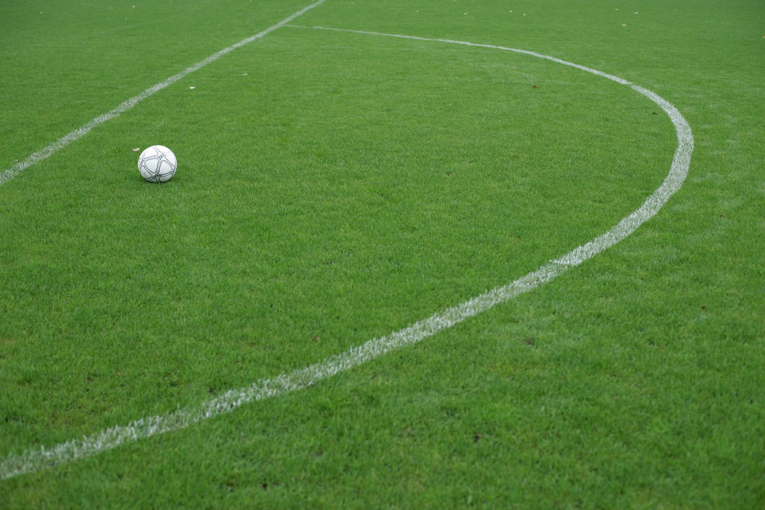 A close-up technical shot of an official tournament soccer ball resting perfectly on the white chalk line of a professional turf pitch