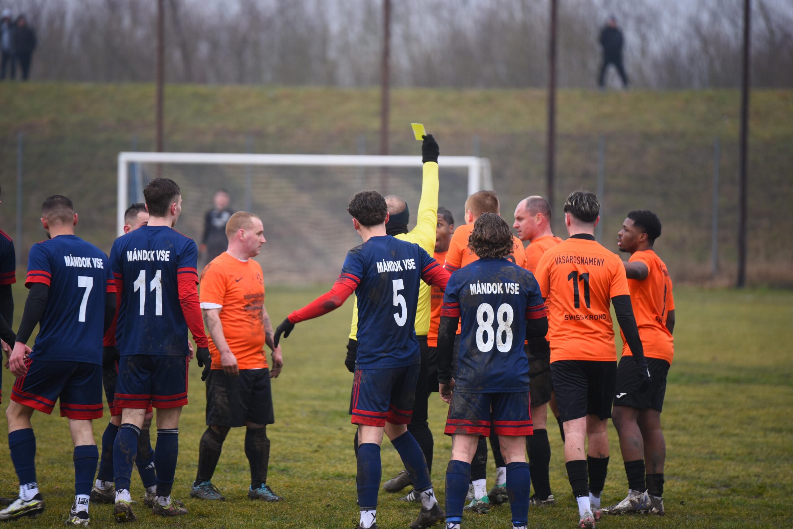 A professional sports editorial photograph displaying an official soccer pitch referee line layout with a grand stadium background under intense athletic lighting