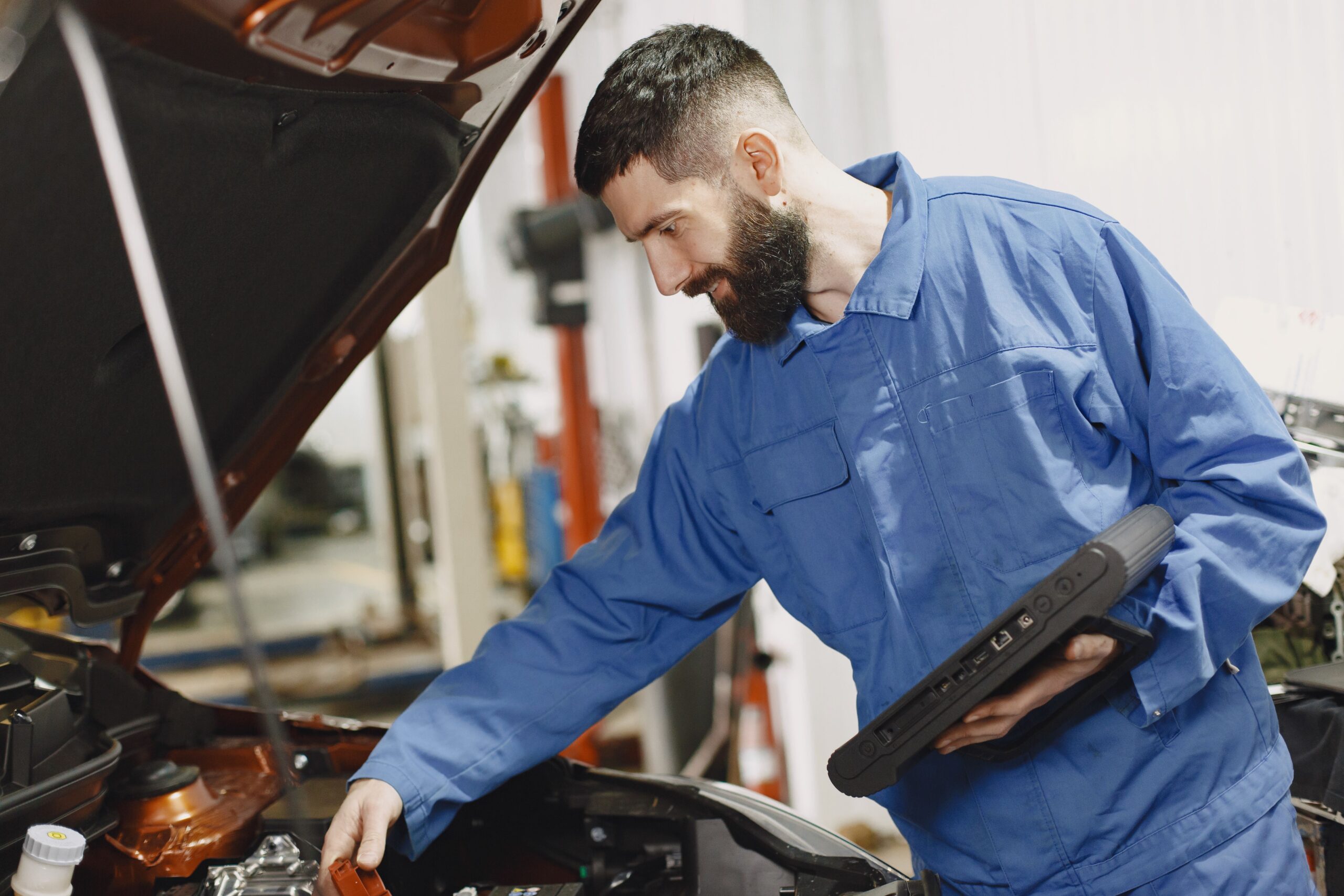 A clean automotive service bay showing a vehicle lifted on a hydraulic hoist with a technician examining diagnostic engine readouts.