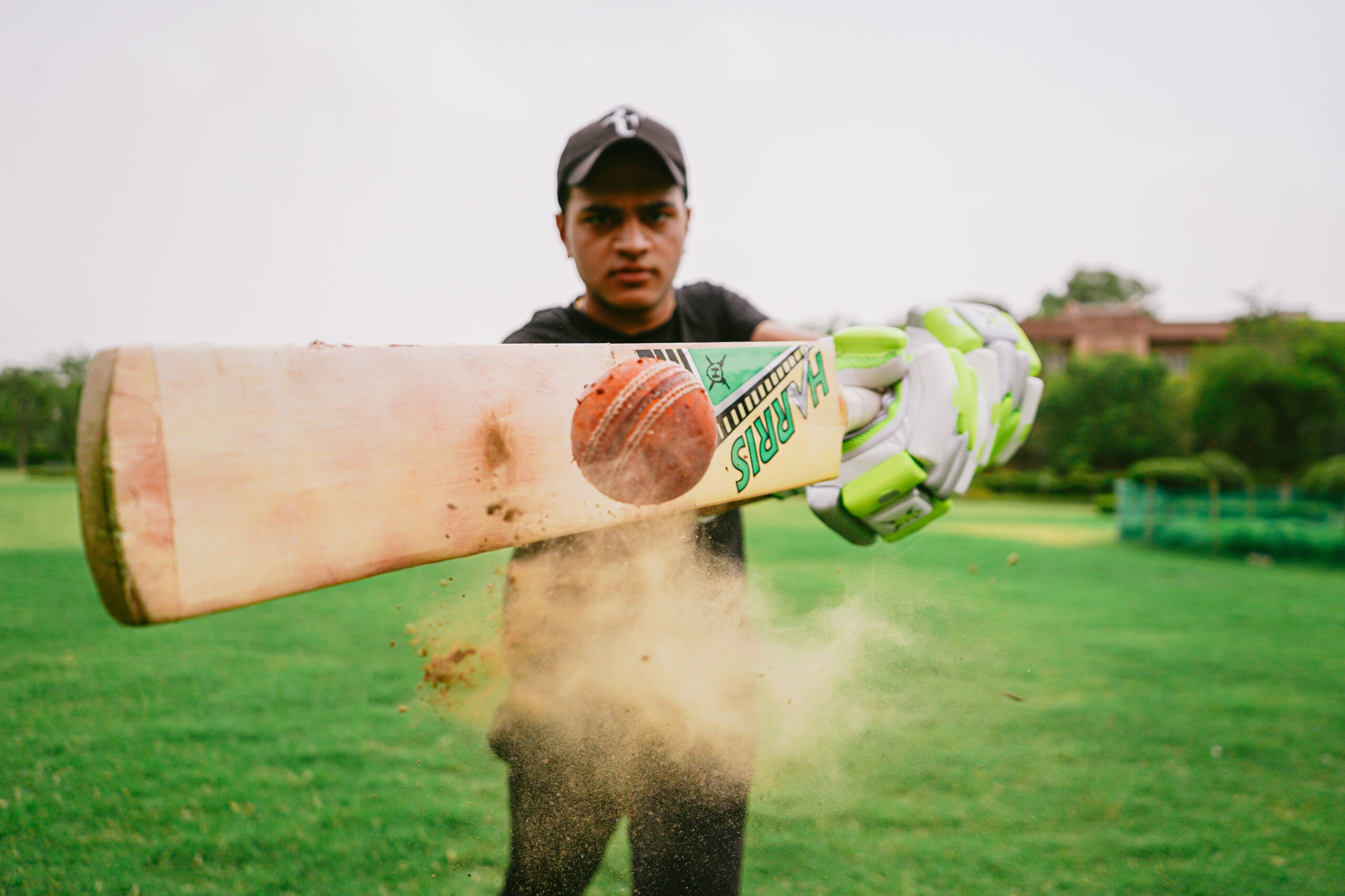 A professional glossy close-up shot of a white cricket leather ball placed next to a modern wooden batting blade on a lush green outfield line