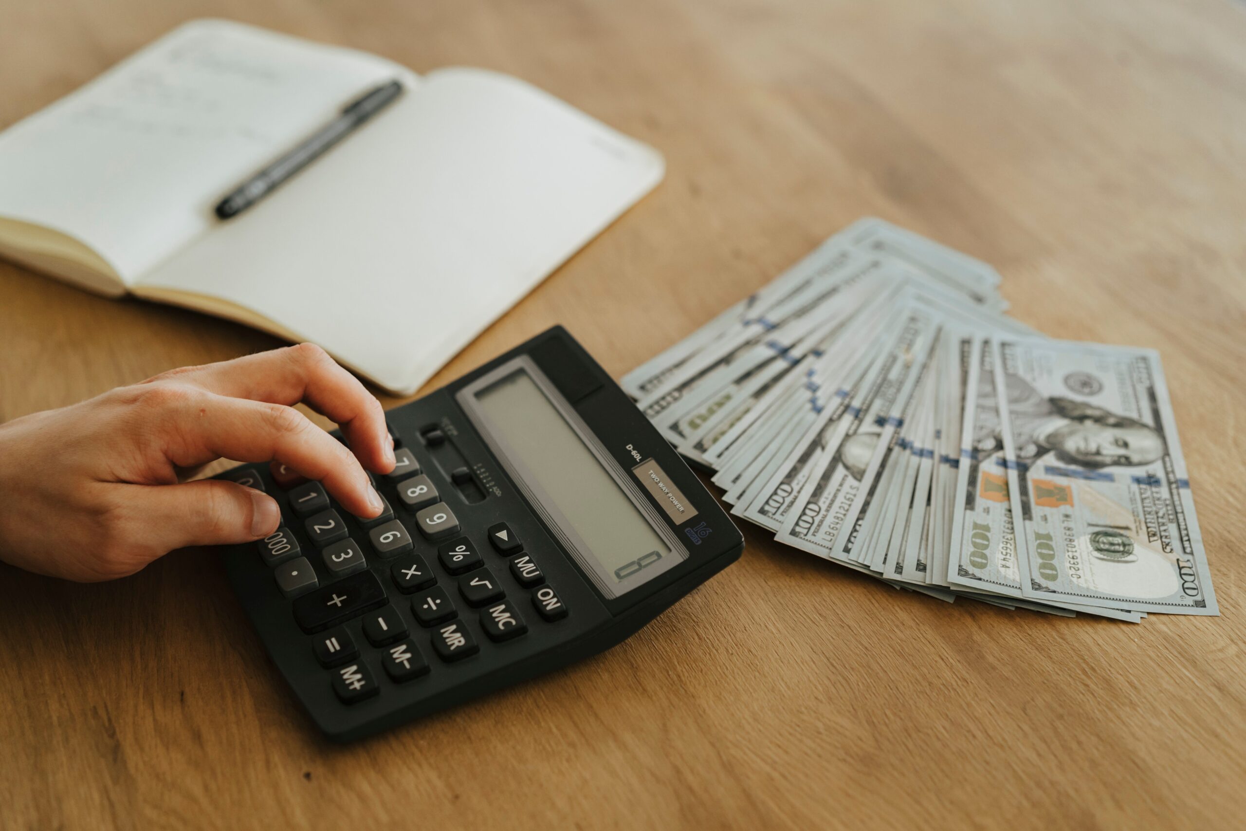 A professional financial journalism photograph showing a modern calculator placed over official United States tax documents and currency on a clean business desk