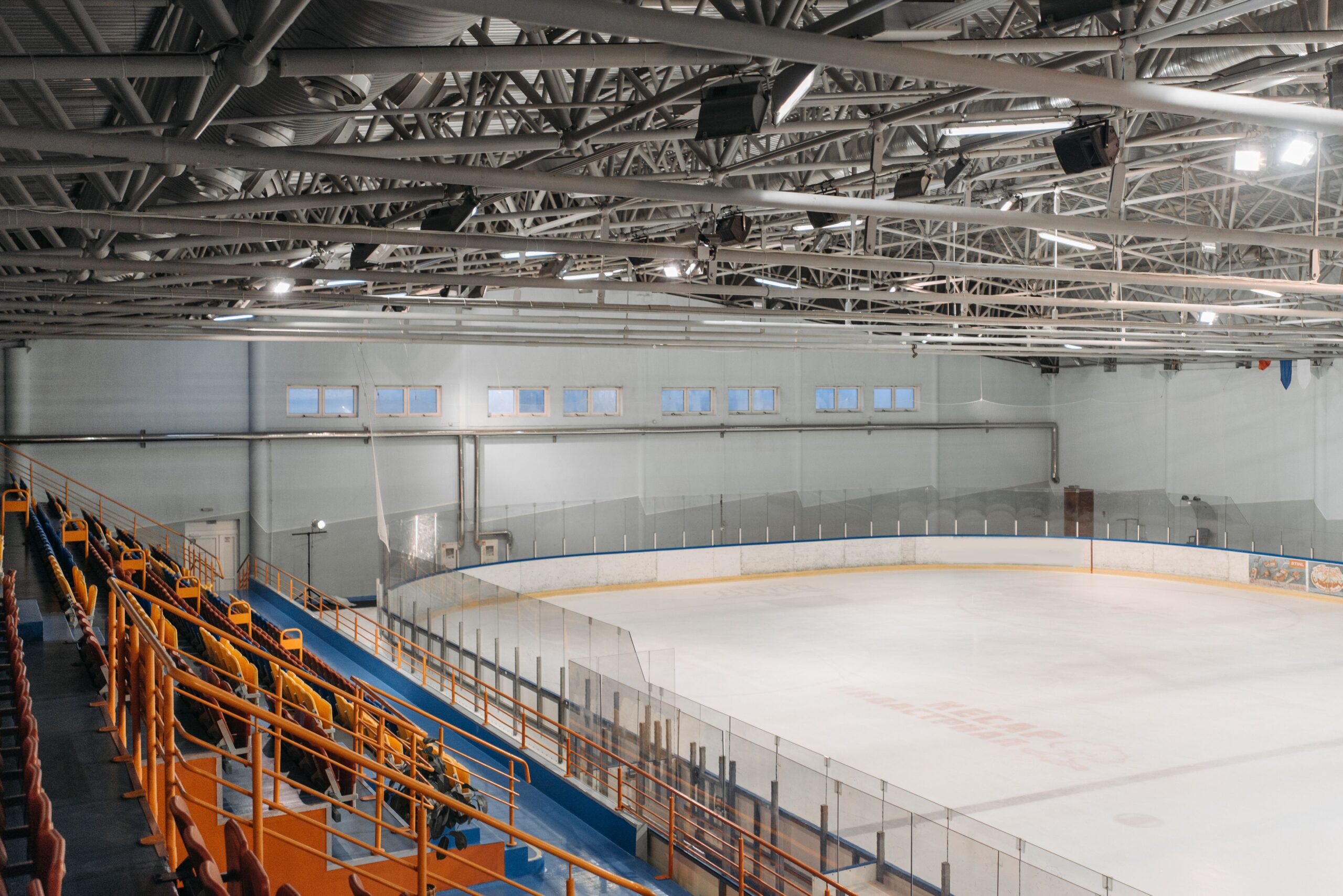 An empty professional indoor ice hockey rink showing crisp red and blue markings with glossy reflective ice surfaces under arena lights.