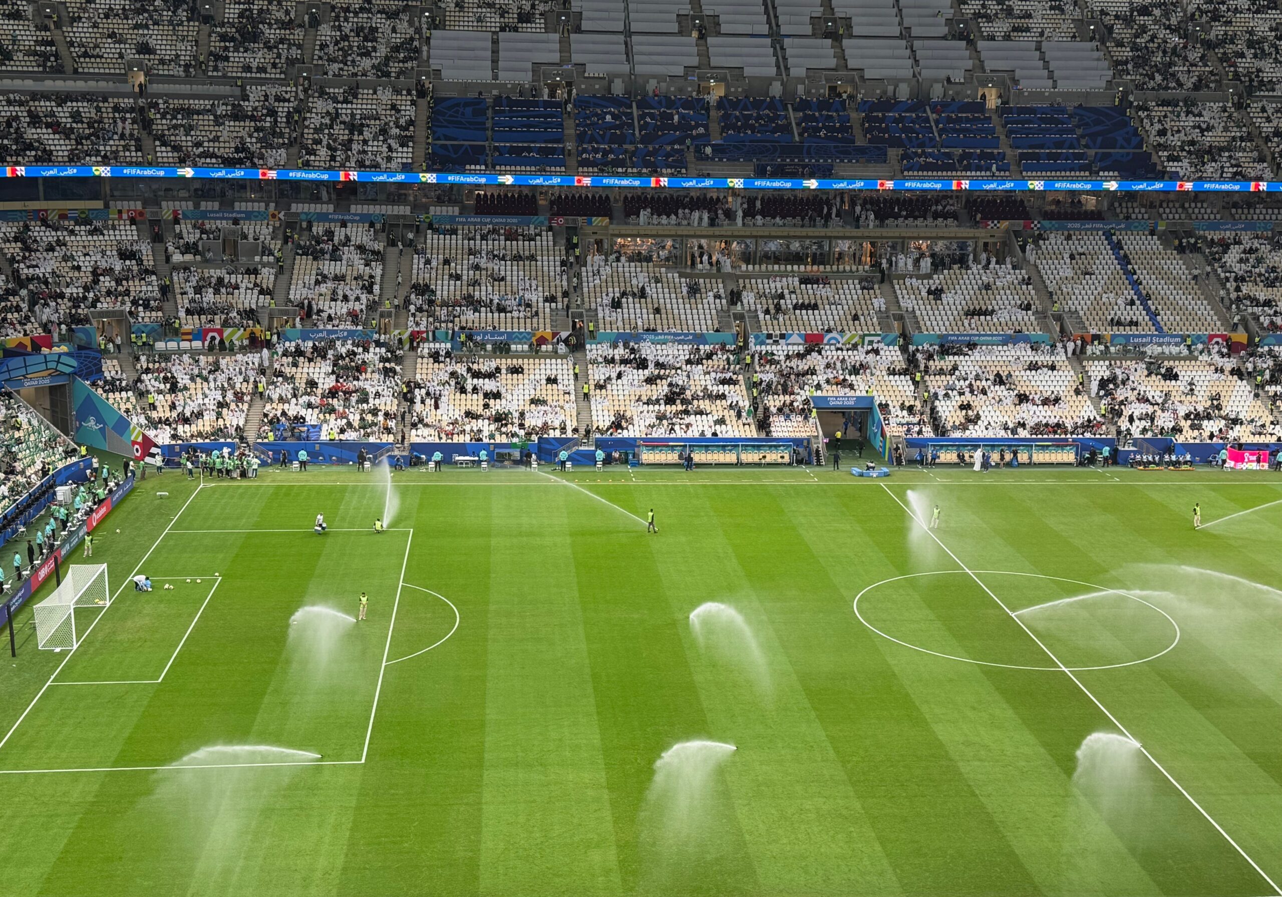 A professional green soccer field turf close-up with a leather match ball sitting under powerful sports stadium lights