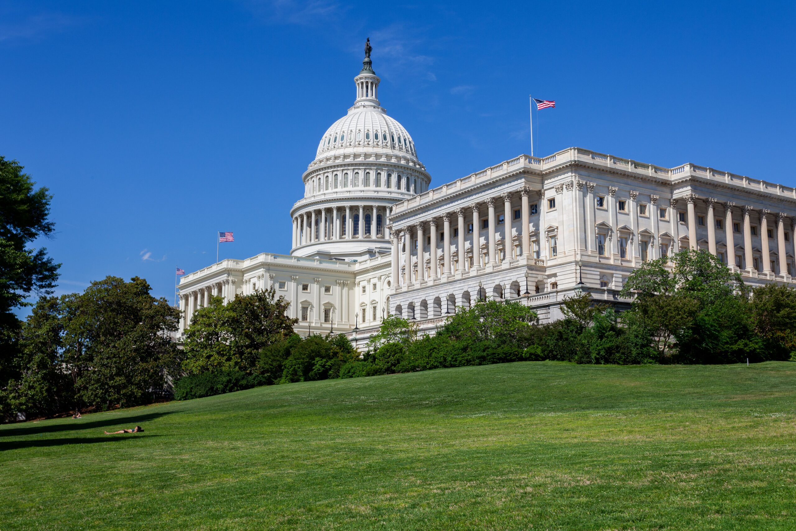 A professional editorial photograph showcasing the grand facade of the United States Capitol building in Washington DC under clear skies