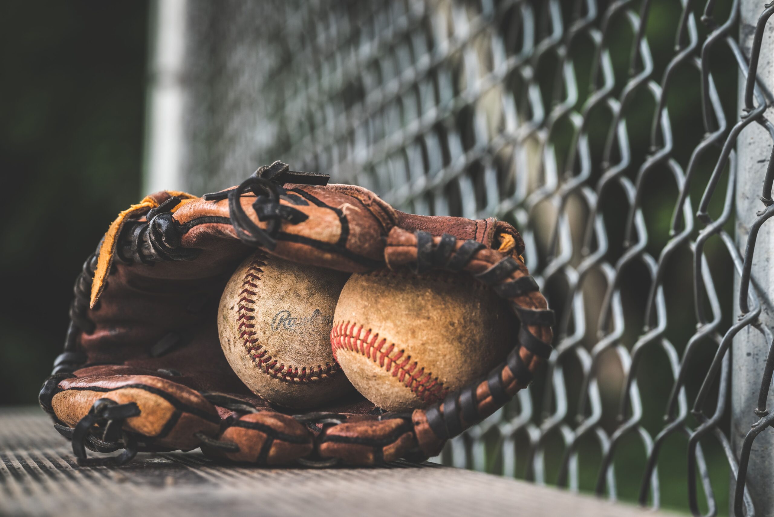 A professional macro photograph of a clean white baseball with red stitching resting on a dark leather glove under bright stadium lights
