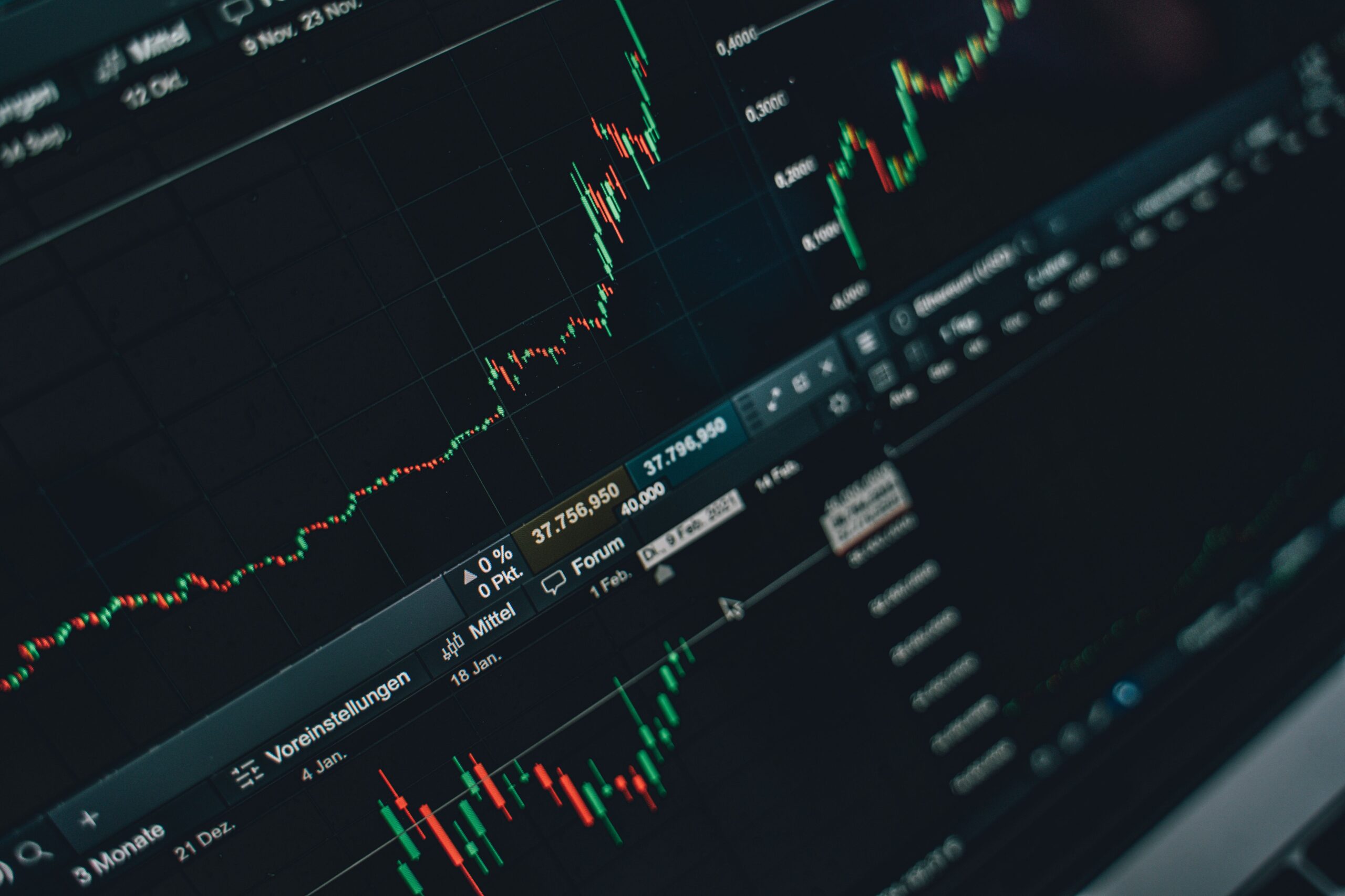 A modern financial workspace with complex green candle stock charts visible on a dual-monitor desktop setup