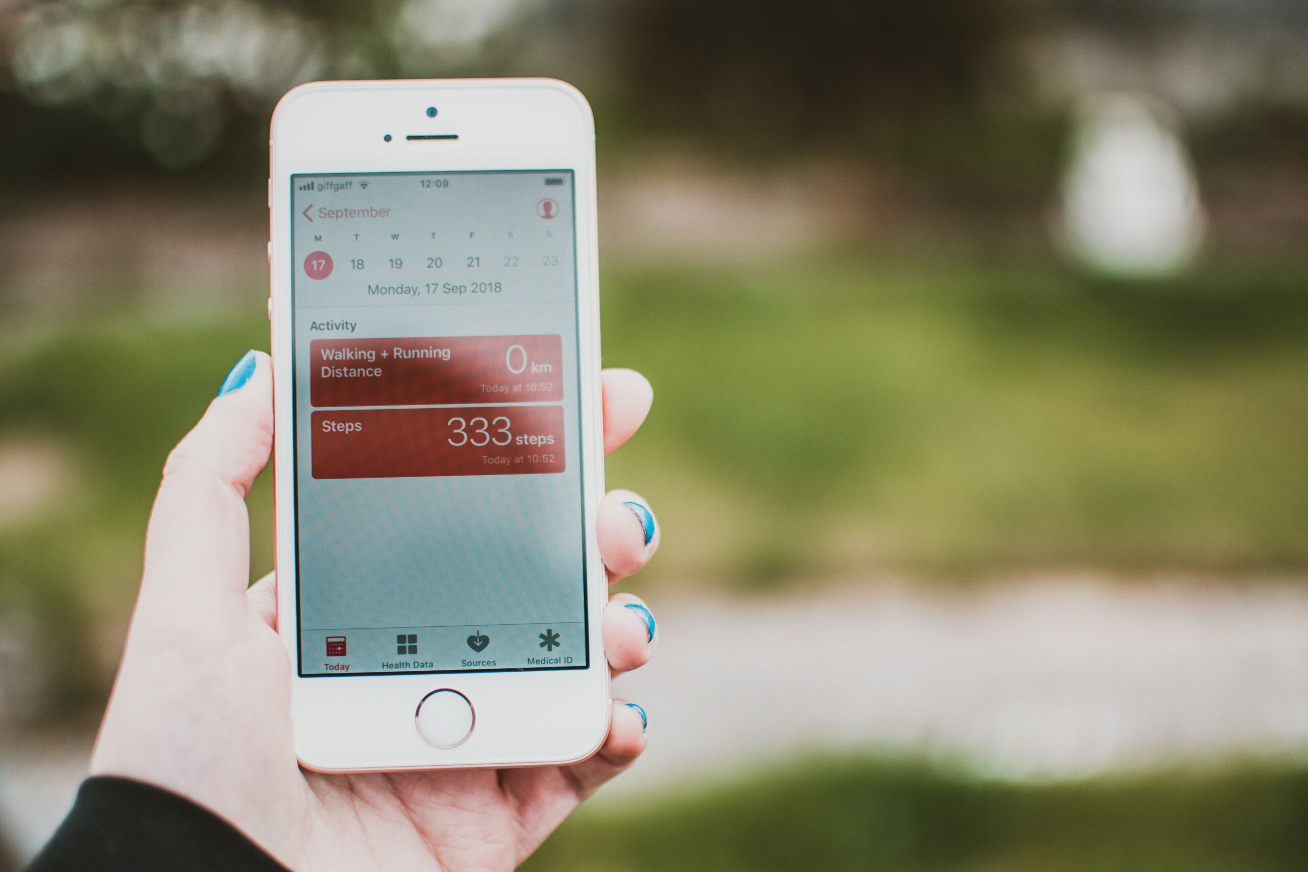 A close-up shot of a smartphone displaying a clean user interface tracking daily walking step count statistics against a green park background
