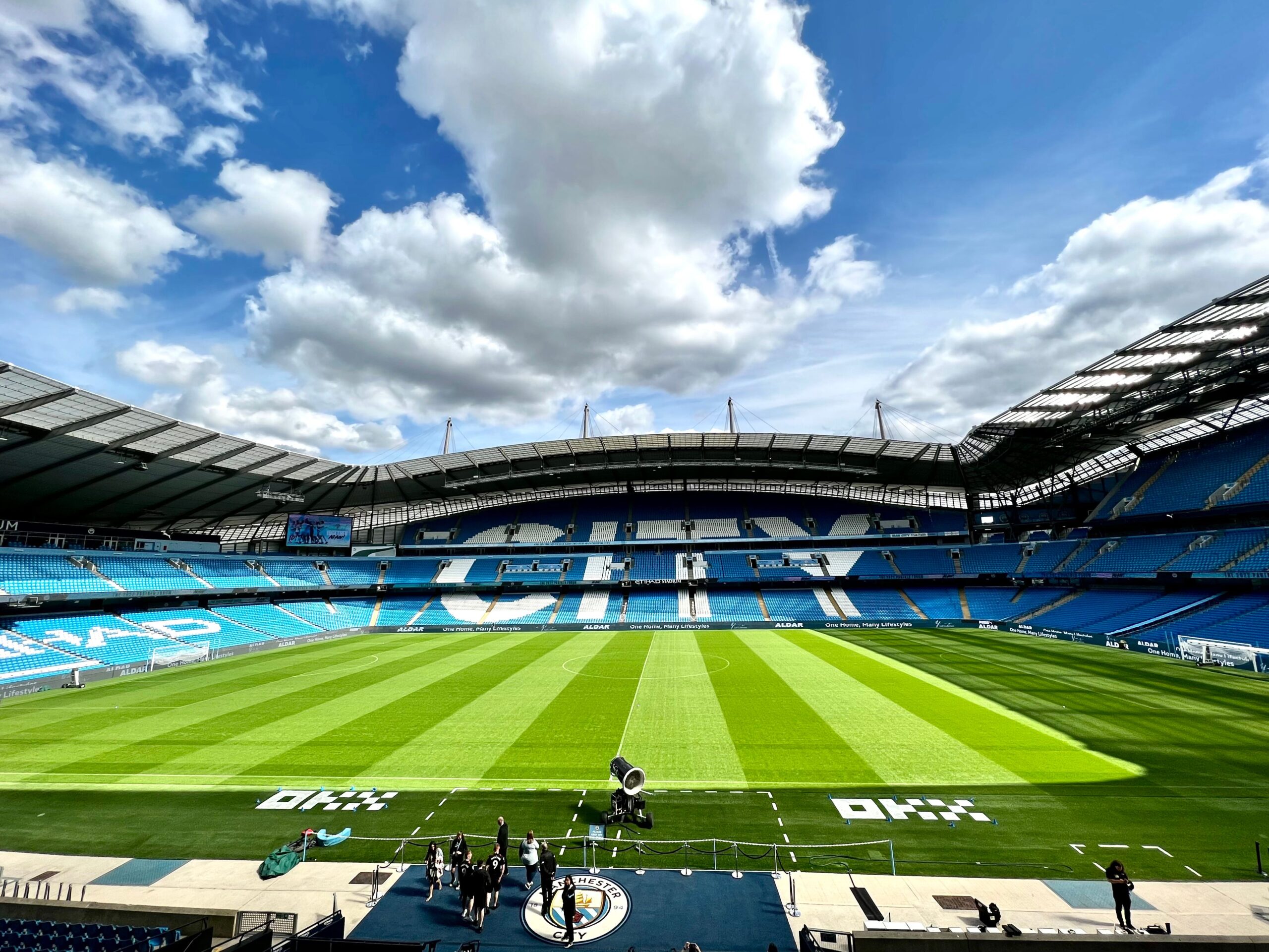 A modern concrete football stadium stands empty under bright floodlights representing a Premier League club venue