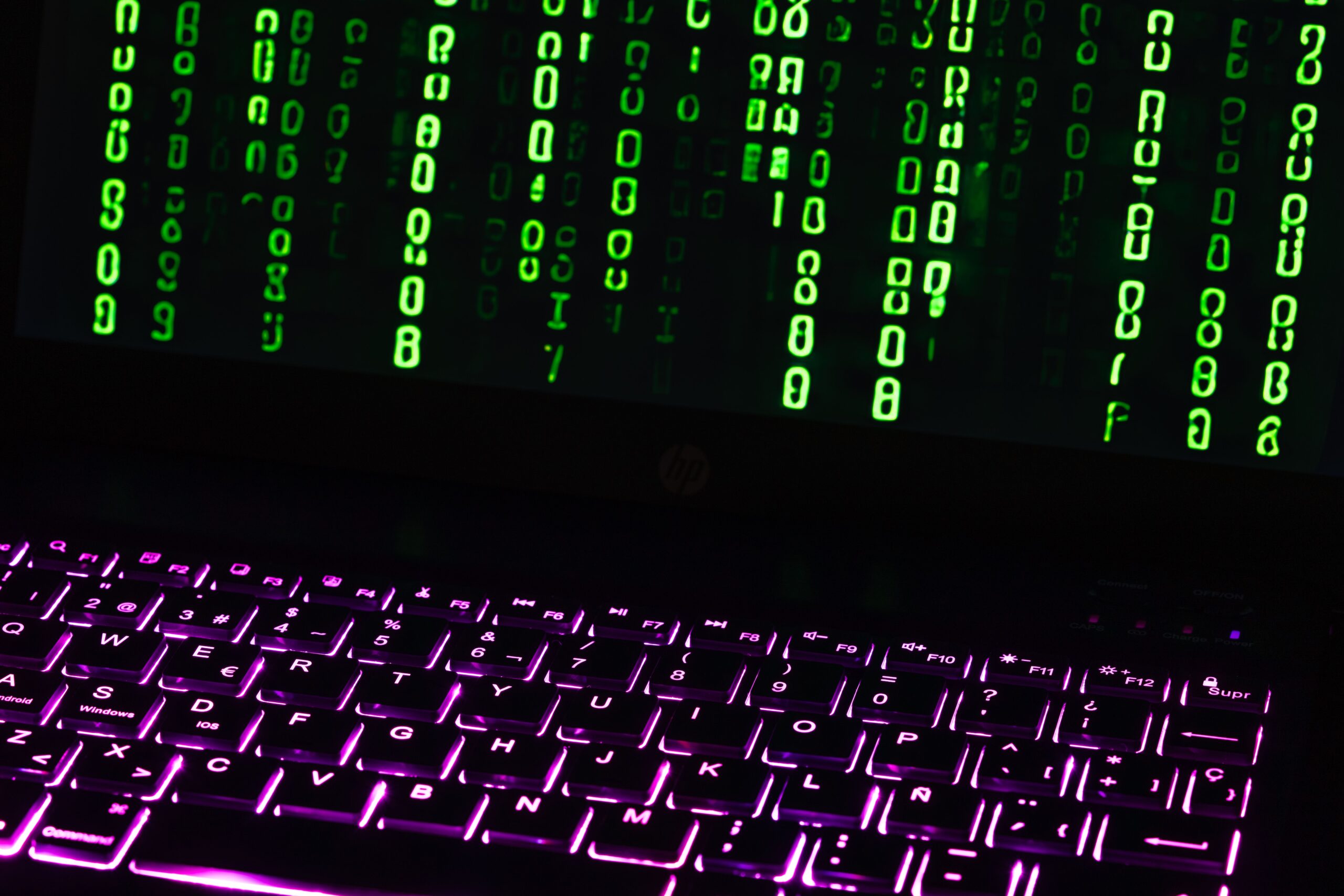 A glowing laptop screen displaying lines of green diagnostic security scripts in a dim room representing a cyber crime unit environment.