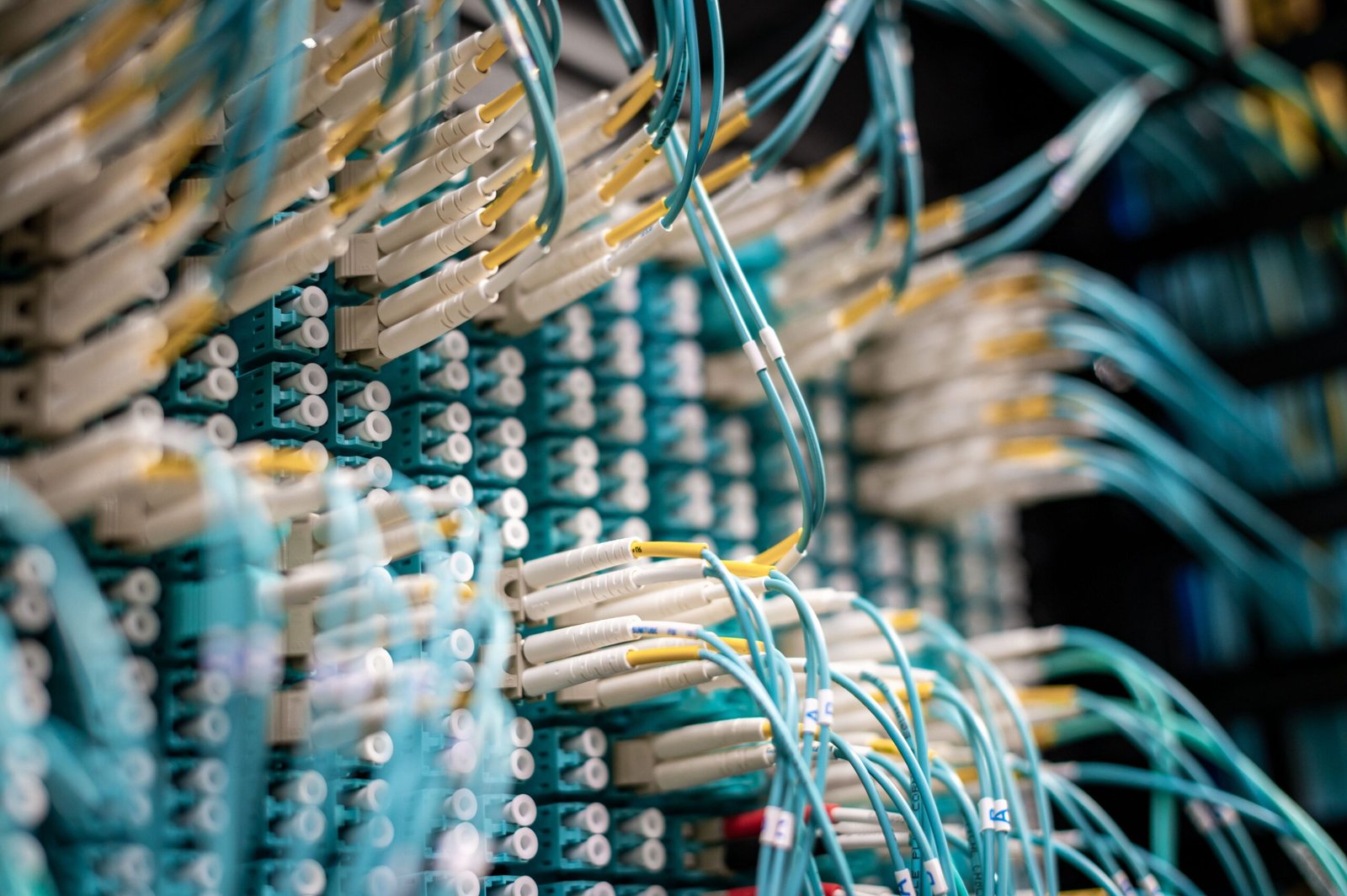 A professional detailed photograph of high-density glowing blue fiber optic networking cables routed inside a server room array.