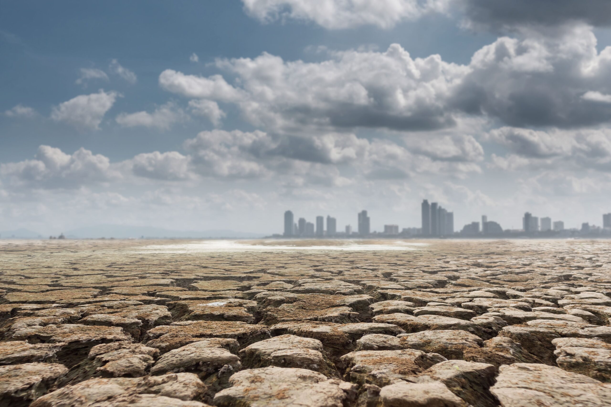 A dramatic high-end commercial photograph showcasing dry, heavily cracked desert ground stretching toward a hazy, burning horizon reflecting extreme climate conditions