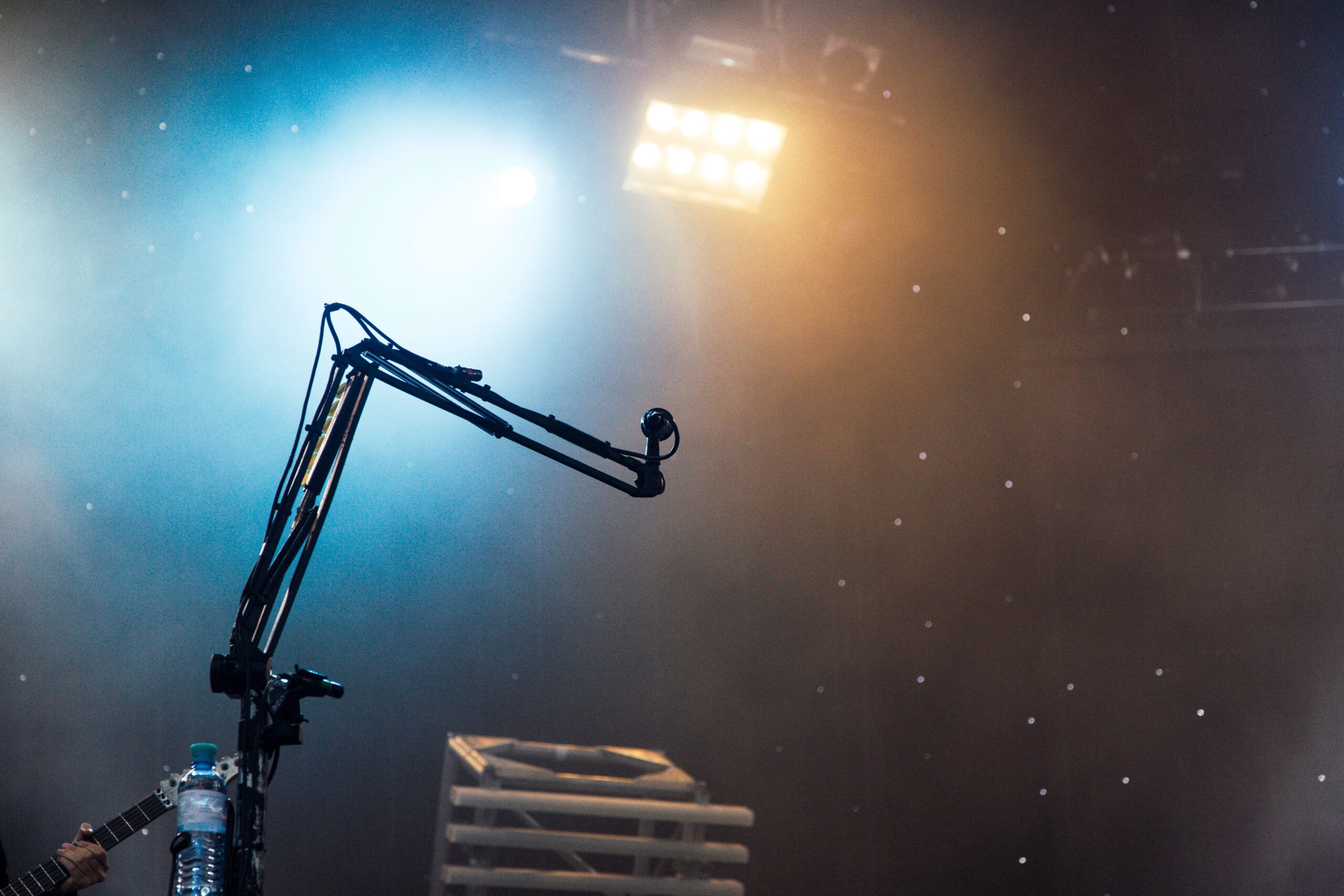 A high-end professional concert stage with bright stadium spotlight rays cutting through a light haze towards an empty microphone stand.