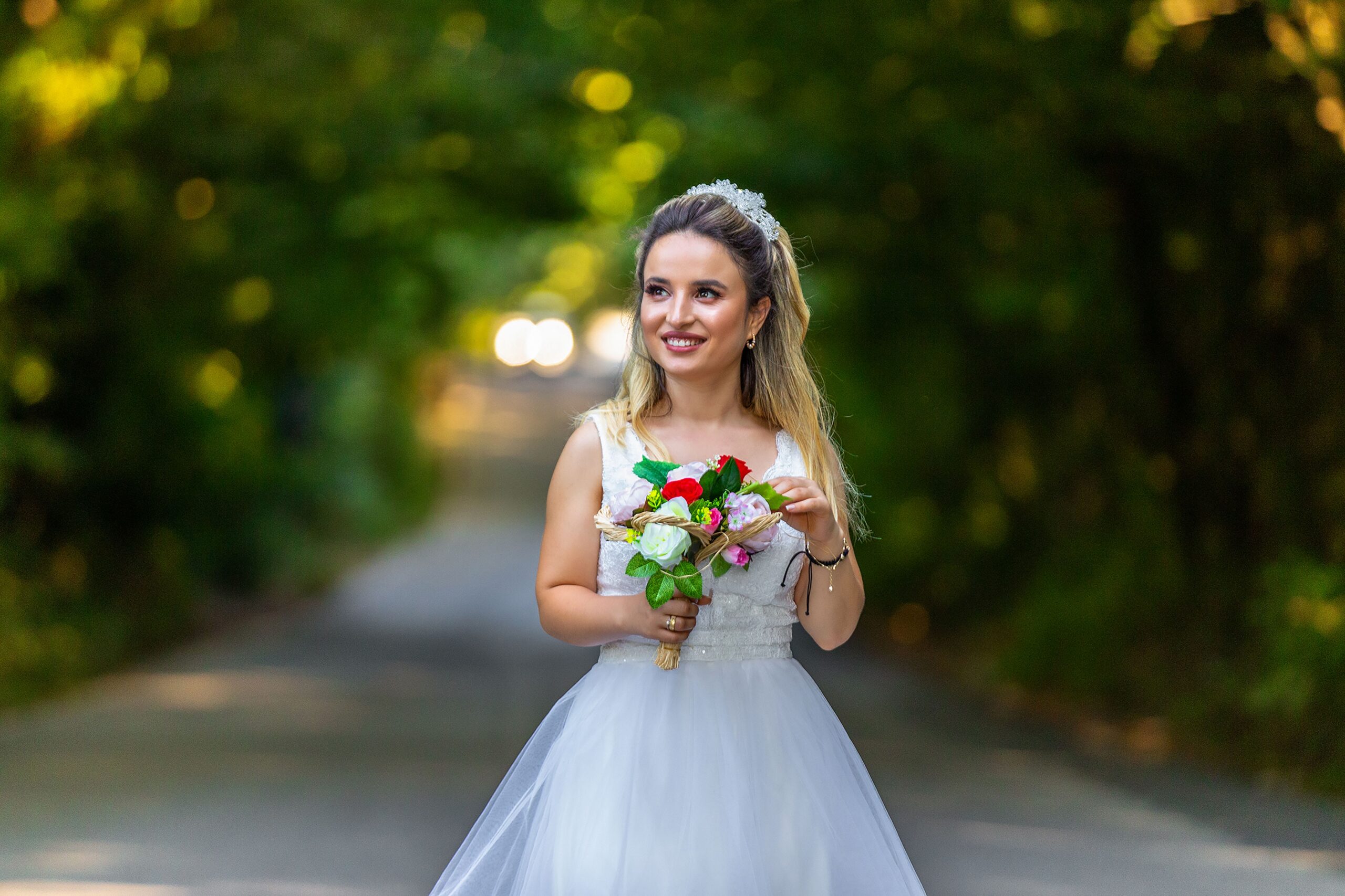 A professional macro photograph focusing on an elegant white bridal bouquet with roses and soft warm blurry background party lights