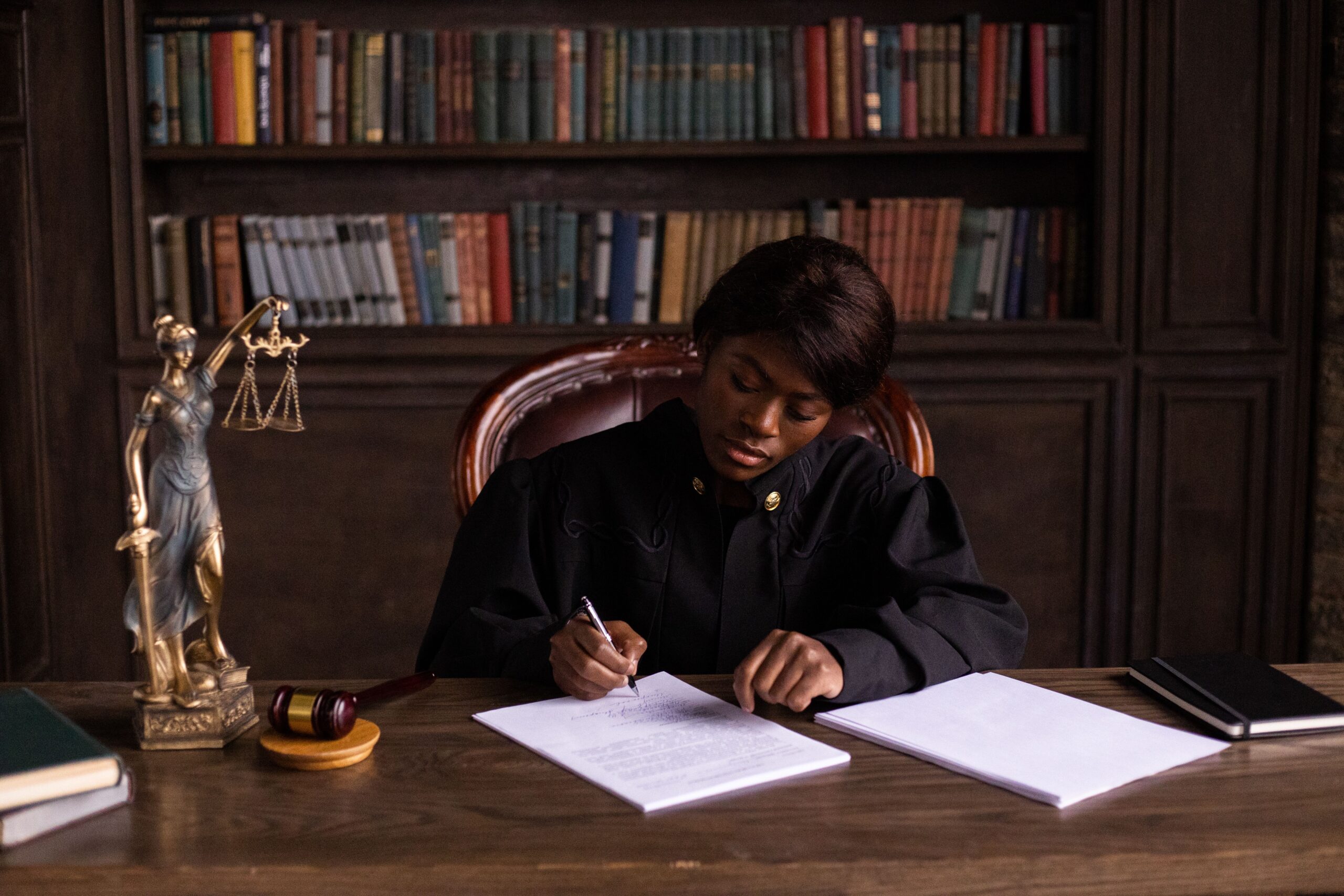 A professional legal journalism photograph displaying a polished wooden judicial gavel resting next to historic statutory law volumes on a dark mahogany corporate desk