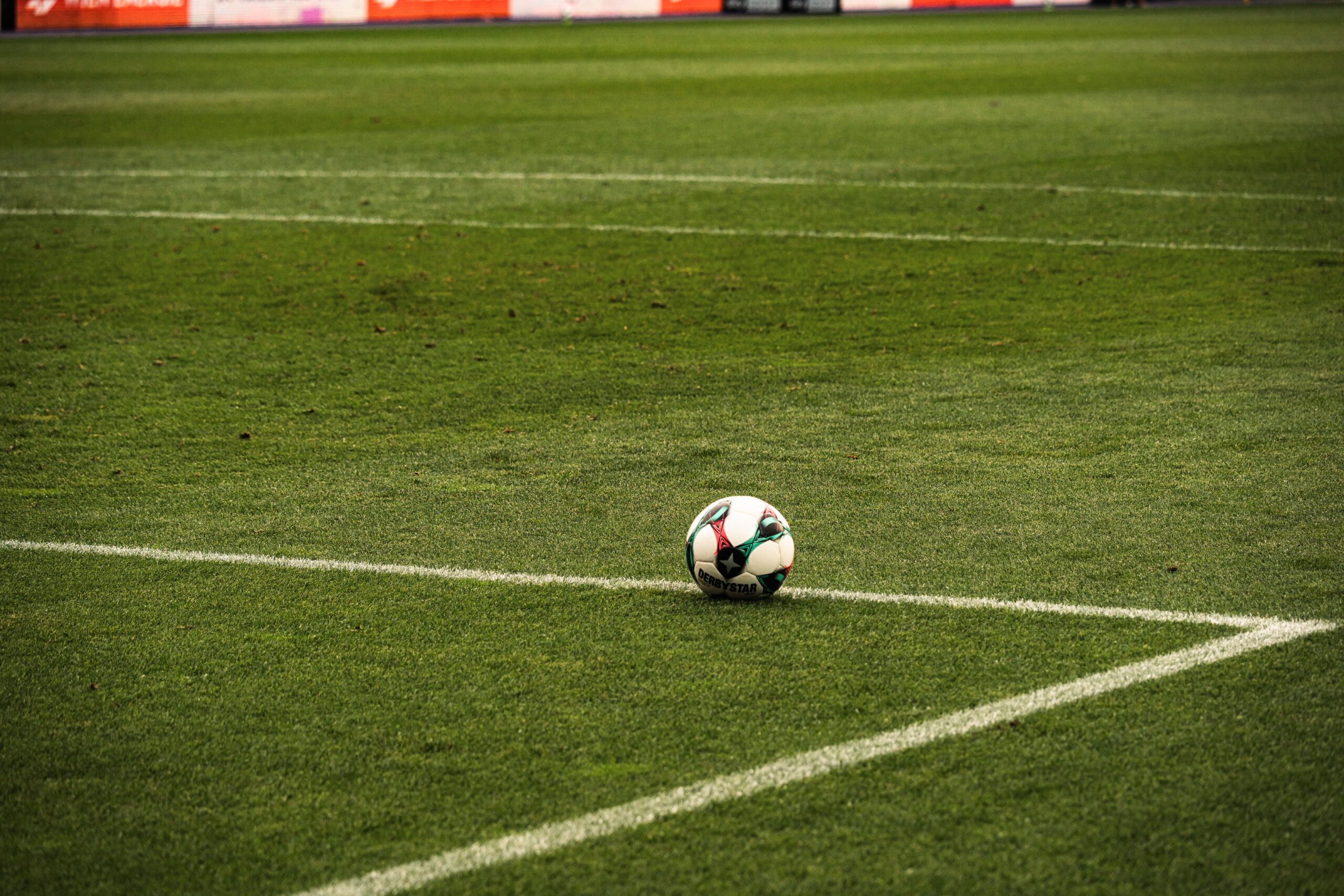 A pristine green professional football stadium turf field shining brightly under giant overhead arena floodlights