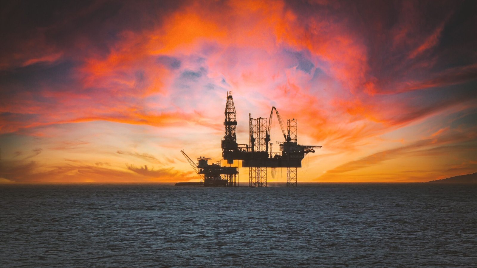 Industrial oil pumpjack operating at sunset alongside financial commodity trading chart indicators